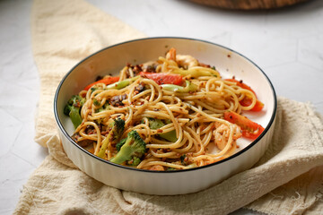 Stir-fried pasta with prawn, broccoli, mushroom and tomato. Served on a white plate.