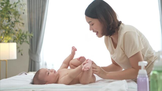 A tiny child smiles happily on the bed waiting for mother apply powder and put on clothes after taking a bath
