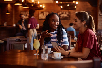 Happy female friends talking while using cell phone in café.