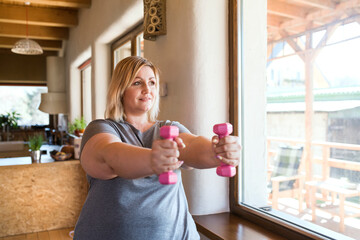Overweight woman exercising at home, using dumbbells. Workout in living room.