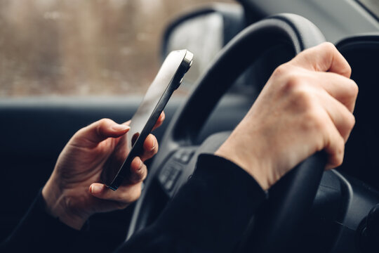 Closeup of female hands typing text message on cell phone while driving car through countryside landscape in winter