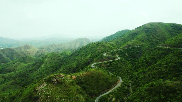 4K shot of vehicles passing on scenic road in mountains and clouds in sky at Rayta in Udaipur, Rajasthan, India. Monsoon clouds and green hills of Rayta. Tourism and holidays background.