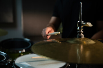 Obraz premium The drummer hits the hi-hat with a drumstick, making a loud, sonorous sound. The drummer is wearing a black shirt, and the cymbal is large and golden. The camera is aimed at the plate in close-up