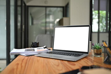 Fototapeta premium Laptop computer with white blank screen and office supplies on wooden table