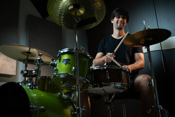 A man plays drums in a recording studio, seated behind a green drum set with black bass drum and two cymbals