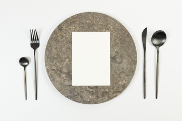 Top view of brown marble plate, black cutlery and white card on white background. Food presentation, stone tray. Table setting, copy space, flat lay.