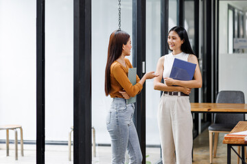 Two Asian businesswomen standing in the boardroom of an office and brainstorming using clipboard notes.