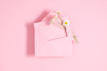 Minimal composition with pink envelope, white blank card and white daisy flowers on pastel pink background. Mockup with envelope and blank card. Flat lay. Top view.