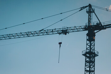 Cranes in the evening sky. Silhouette of a crane and part of a building under construction with blue sky. 