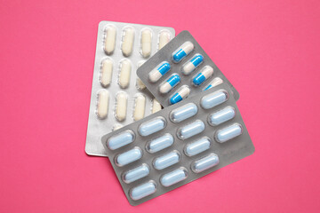 Different antibiotic pills in blisters on pink background, top view