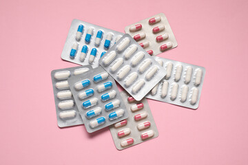 Antibiotic pills in blisters on pink background, top view