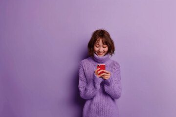 Satisfied smiling woman reads great message in her smartphone isolated on purple pastel background.