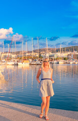 Greece. Rethymnon. Crete. A woman is standing gracefully by the marina at sunset, with beautiful boats in the background