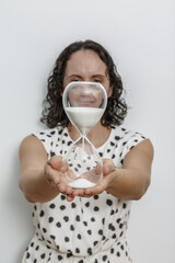 Woman Holding Glass Hourglass While Wearing Polka Dot Dress Against White Wall