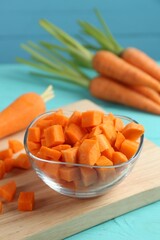 Delicious chopped carrot in bowl on light blue wooden table, closeup