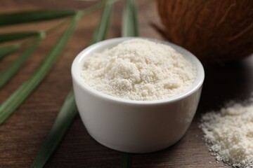 Organic coconut flour in bowl on wooden table, closeup