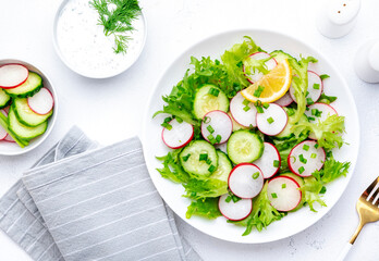 Summer vegan crispy salad with cucumbers, radishes and lettuce, white background, top view