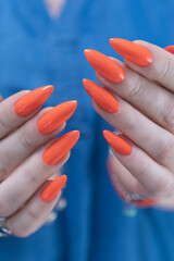 Woman hand with long nails and light orange red neon manicure