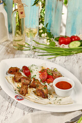 Pork Shashlik with Lavash, Sauce, and Vegetable Salad under Sunlight on Wooden Table