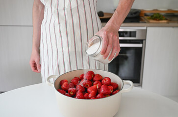 person sprinkles sugar on strawberries, making sweet strawberry jam