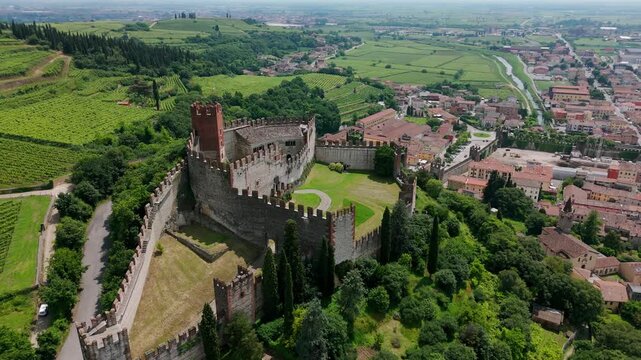 Aerial view of the historic Soave Castle surrounded by lush greenery and vineyards in Italy. orbit motion shot