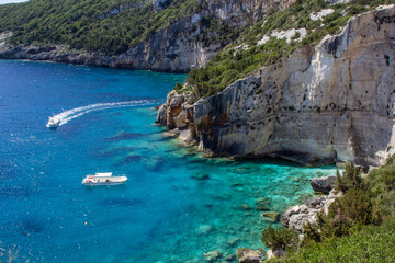 Obraz premium Boats on Crystal Clear Waters Along Rocky Coastline in Greece