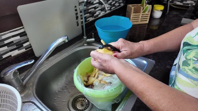 A woman's hands are peeling potatoes over the kitchen sink, peeling vegetables for cooking in the kitchen. Water flows from the tap. High quality 4k footage
