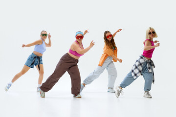 Naklejka premium Young girls, dancers strike dynamic pose in colorful outfits and sunglasses, shows their individuality and energy against white studio background. Concept of music, fashion and art, sport and hobby.