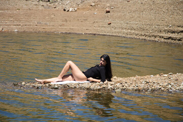 beautiful young brunette latin woman in black shirt and black bikini lying relaxed on the shore of...