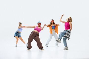 Naklejka premium Group of four dancers in vibrant, casual outfits and sunglasses strikes pose, reflecting their energetic and playful dance style against white background. Concept of fashion and art, sport and hobby.