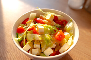 Close-up of vegetable salad in the bowl on the kitchen table. Tomatoes, feta cheese, chicory, onions, dressing and olive oil. Healthy food, tasty salad, raw vegetables.