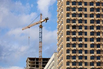 Fototapeta premium Tower crane and unfinished buildings on background of blue sky. Housing construction, apartment blocks in city