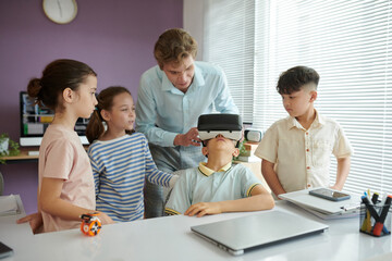 An instructor guiding group of children through virtual reality experience in modern classroom with various devices around them.