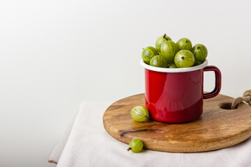Fresh green gooseberry berries in a red enamel mug