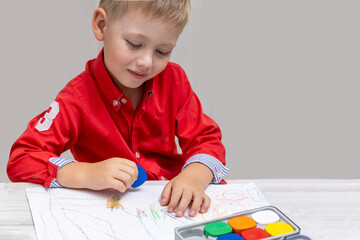 A toddler drawing with wax crayons on paper in a child's room, sitting at a table