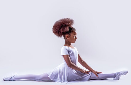 Ballerina in a white leotard. Little ballerina girl laying on the ground. Flexible little african american girl ballerina. Ballerina in dance class. Kids practice full split