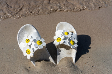 Colorful flip flops with the flowers on the sandy beach.