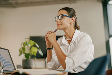 A Professional Woman Sitting in the Office Deep in Thought Within a Contemporary Workspace
