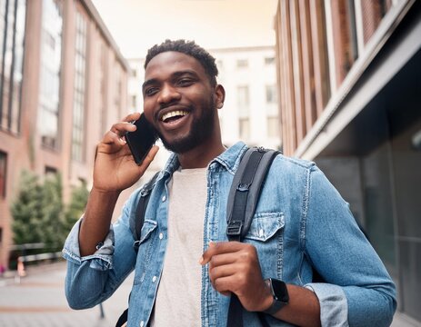 Happy young African Black man hipster or tourist with backpack standing on city street outdoors holding smartphone talking on mobile cell phone having conversation making call on smartphone.
