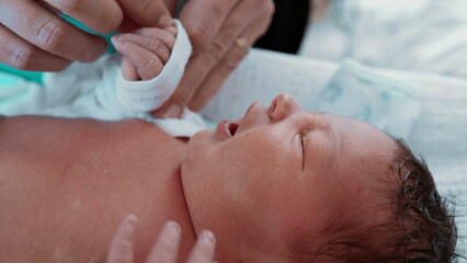Newborn Baby - Mother Dressing Infant's Hands, Close-Up. A tender moment showing a mother dressing her newborn son's tiny hands, highlighting the nurturing bond between mother and child