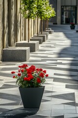 A contemporary grey pedestrian street with geometric pathways and grey benches is punctuated by a single, vividly colored red flower pot, providing a focal point in the monochromatic setting.