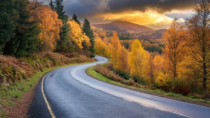 Fototapeta premium Winding road through autumn forest with mountains and dramatic sky