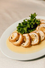 Delicious cheese rings with aromatic fresh herbs under a creamy sauce on a beautiful white plate in a cozy and nice restaurant