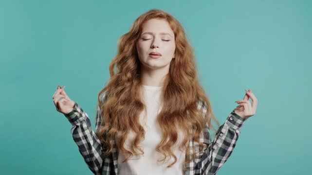Tranquil woman relaxing, meditating, refuses stress. Ginger lady breathes deeply, calms down, blue studio background. Yoga, moral balance, zen concept.