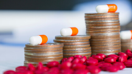 White and orange capsules on a pile of coins and pills, meaning health insurance, medical expenses...