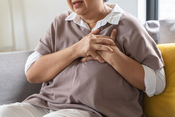 Obraz premium Asian elderly grabbing her chest and feeling pain from heart attack suddenly at home.