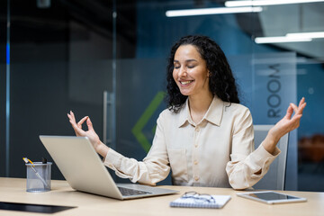 Calm businesswoman meditating at office desk with laptop and notepad. Employee finding balance and reducing stress during work. Office environment fosters relaxation and focus