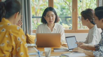 Obraz premium A team meeting in a bright office with colleagues engaged in discussion, focusing on a woman speaking prominently at the head of the table.
