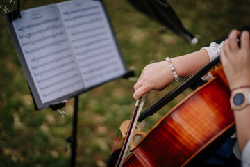 Cesis, Latvia - July 12, 2024 - Close-up of a musician playing a cello outdoors, with a sheet music stand in the background, focusing on the bow and arm movement. © Raivo