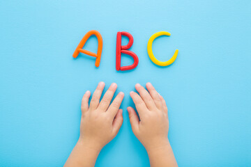 Baby boy hands and colorful abc letters created from modeling clay on light blue table background. Pastel color. Time to learning. Closeup. Point of view shot. Top down view.